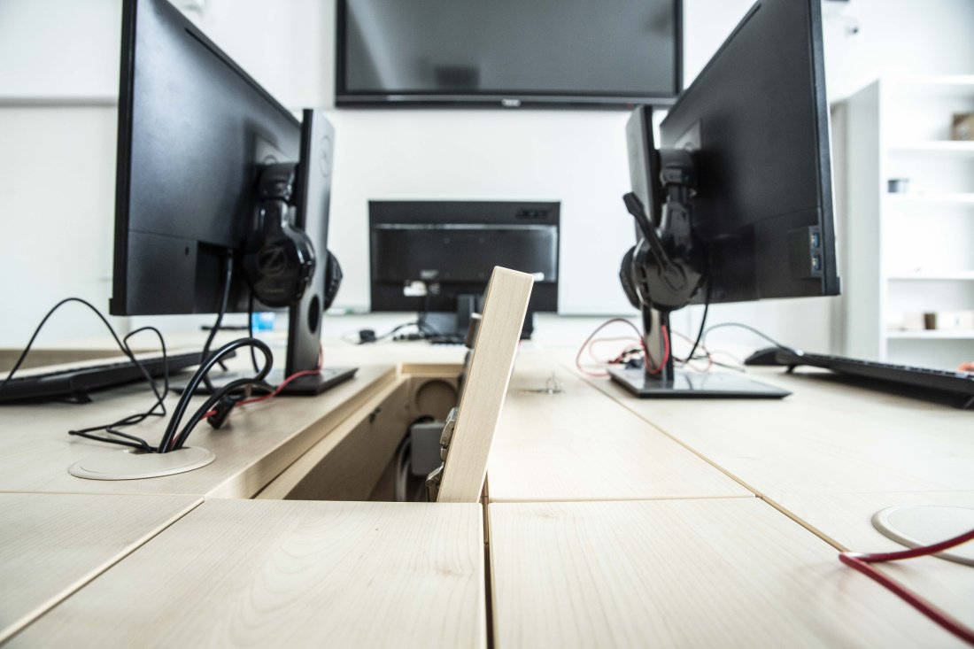 Detail počítačových stolů s kabelovými průchodkami mezi monitory.