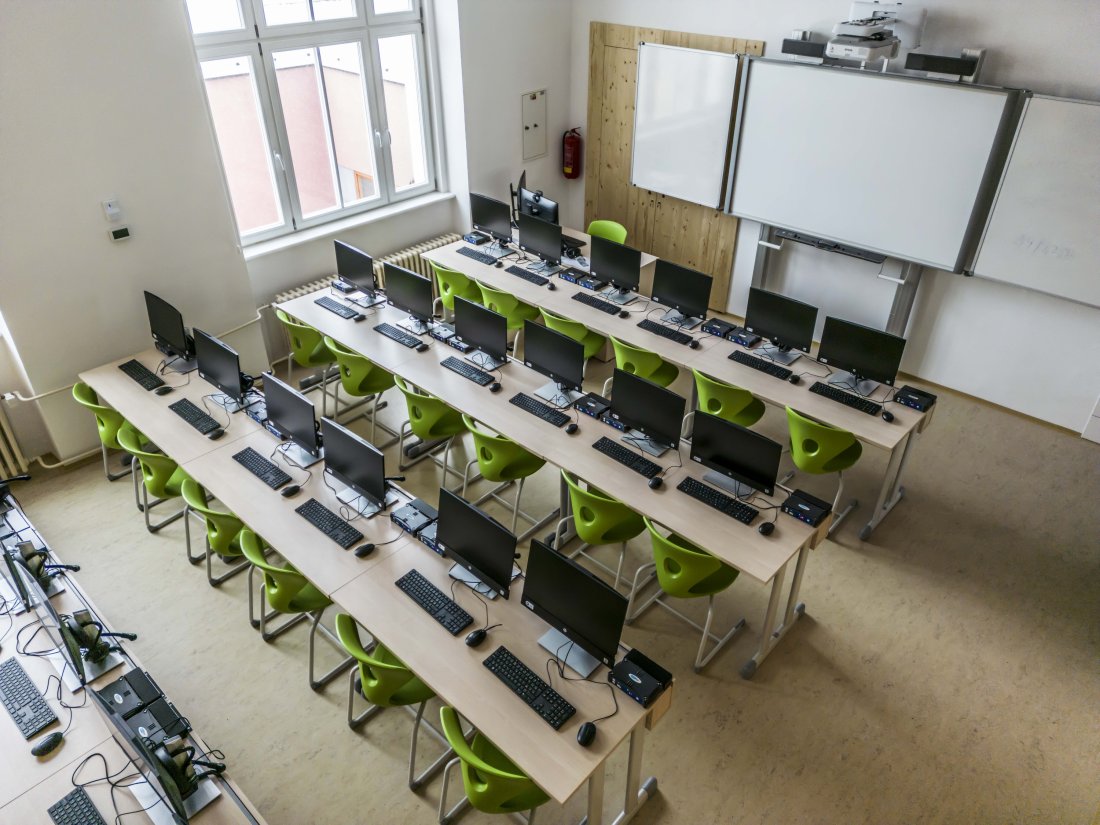Řady počítačových stolů směřující k tabuli v přední části učebny